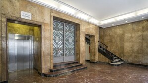 Un vestíbulo con piso de mármol, un ascensor, una escalera y una puerta de vidrio decorativa.