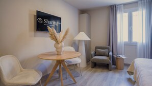 Habitación de hotel con una mesa redonda de madera, dos sillas, un sofá, una lámpara y un cartel en la pared.