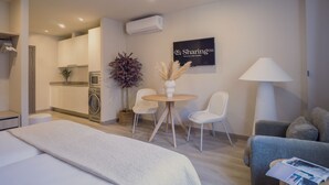 Una habitación de hotel moderna con una cama, una pequeña mesa redonda con sillas, un sofá, una lavadora y un cartel que dice 'Sharingco'.