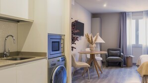 Un espacio habitable compacto con área de cocina, una mesa de comedor con sillas, un sofá y un televisor montado en la pared.