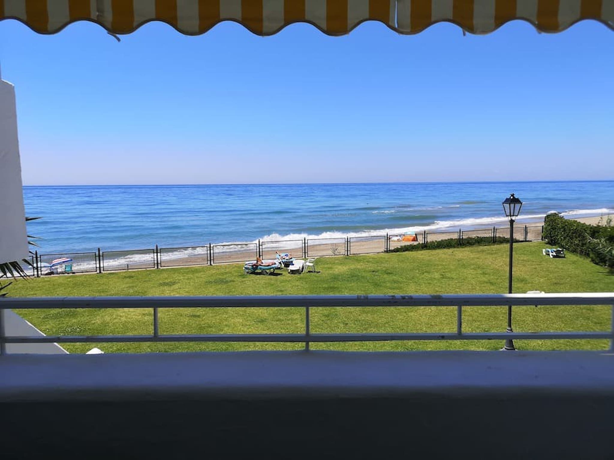 A balcony with a view of the ocean, a grassy area, and a lamp post.