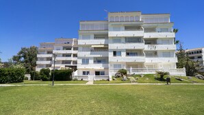 A multi-story residential building with balconies, a grassy front yard, and a clear blue sky. - Amazing flat with views & pool by SharingCo  (Marbella)