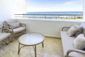 Ein Balkon mit Korbmöbeln, einem Glastisch und Blick auf das Meer.
