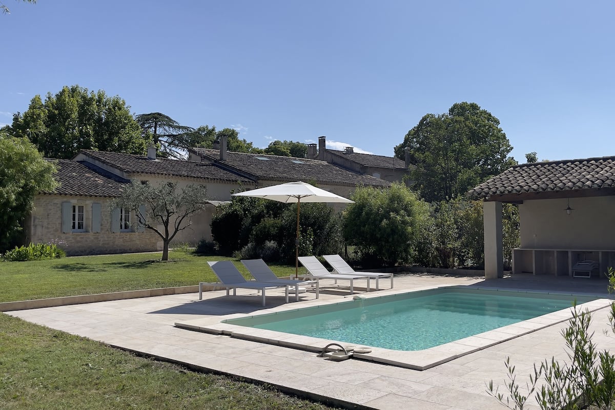 Una piscina rectangular con un borde de azulejos, rodeada por dos tumbonas y una sombrilla.