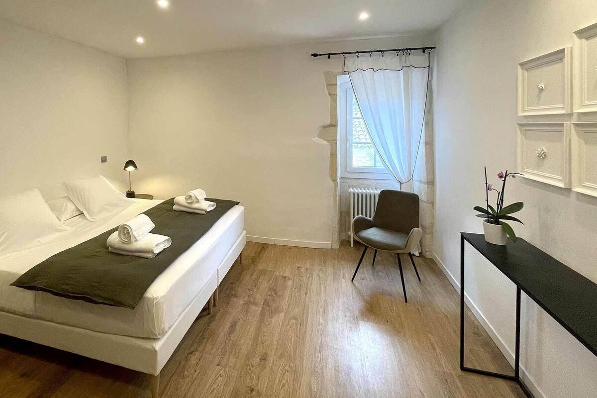 Una habitación de hotel moderna con una cama, una silla, una mesita y un ventanal con cortinas.