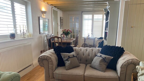 A cozy living room with a beige sofa, wooden flooring, and a dining area in the background.