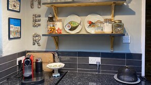 A kitchen with granite countertops, a coffee maker, a fish-shaped plate, and decorative jars on a wooden shelf.