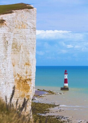 A coastal scene with a white cliff, a red and white lighthouse, and a clear blue sky. - Beautiful Seaside Cottage  (Seaford)