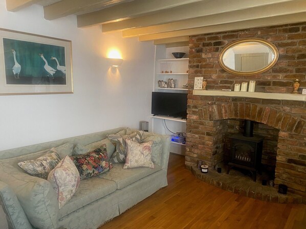 A cozy living room with a sofa, a fireplace, a TV, and a framed picture on the wall. - Beautiful Seaside Cottage  (Seaford)