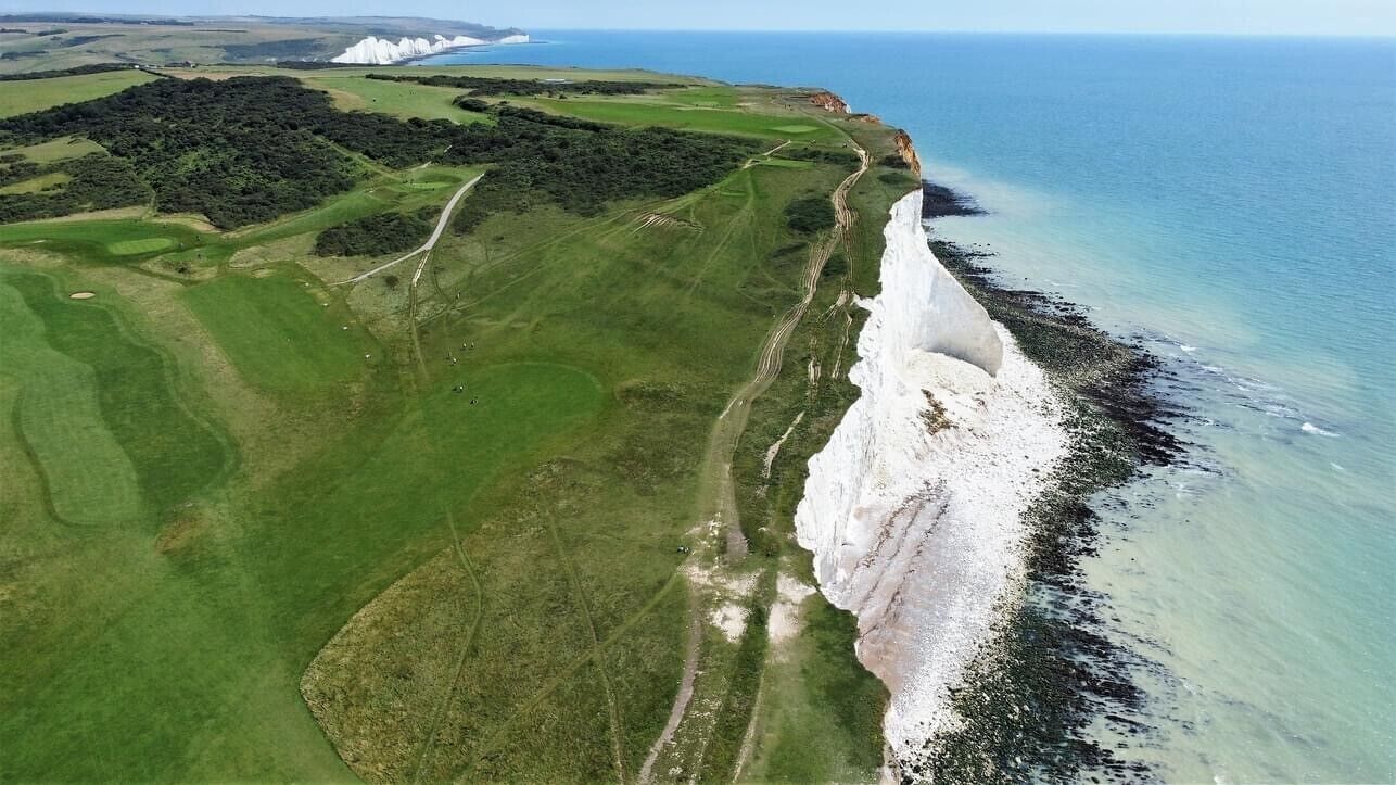 An aerial view of a coastal area with a golf course, a white cliff, and the ocean.