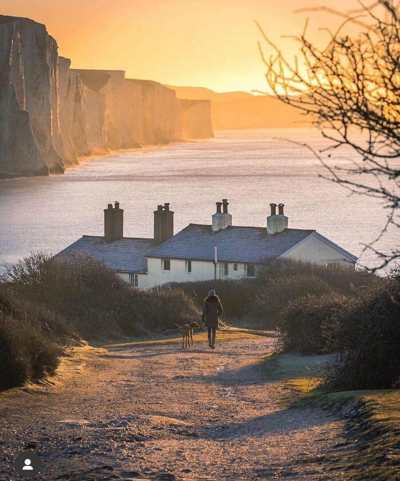 Una casa costera con un camino empedrado que lleva a la entrada, con vista al mar y los acantilados.