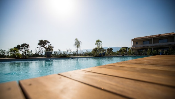 Eine Holzterrasse führt zu einem Schwimmbecken, mit freiem Blick auf Bäume und ein Gebäude im Hintergrund.