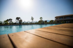 A wooden deck leading to a swimming pool with a clear view of trees and a building in the background. - Résidence Saint Cyprien Plage (Lecci)