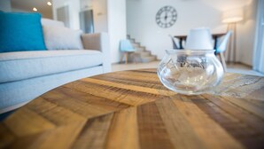 Ein modernes Wohnzimmer mit einem Holztisch, einer Glasvase und einem weißen Sofa mit blauen Kissen.