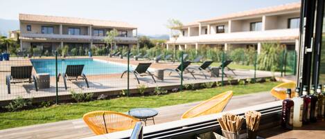 A view from a hotel room overlooking a swimming pool with lounge chairs and a wooden deck.