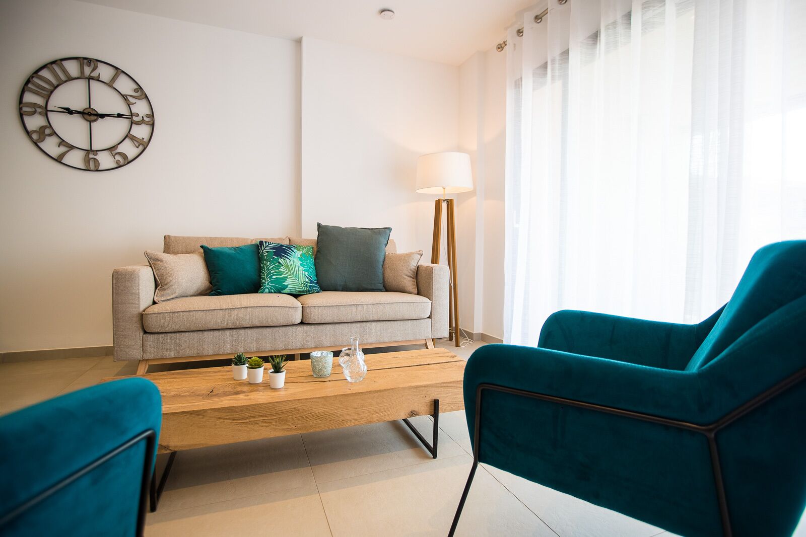 Una sala moderna con un sofá, sillas color turquesa, una mesa de centro y un reloj de pared.
