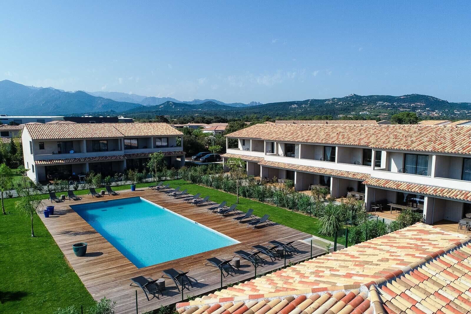 A resort with a swimming pool, lounge chairs, and a view of mountains.