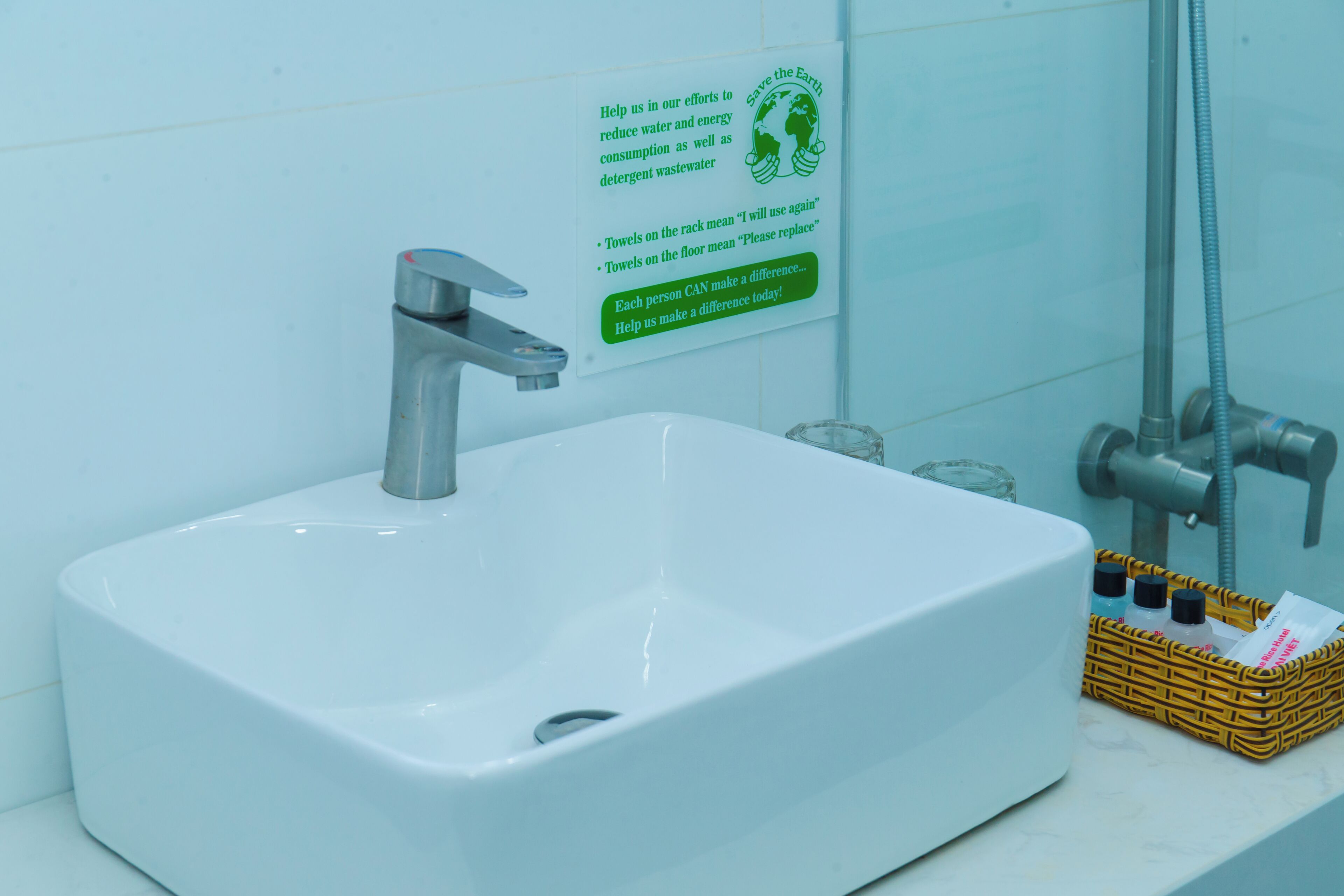 Un lavamanos con grifo, un vaso de agua y un cartel sobre el ahorro de agua.