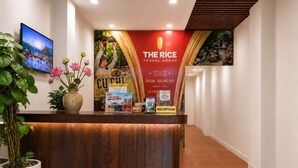 A reception desk with a wooden finish, a potted plant, and a wall with a travel group advertisement. - The Rice Hotel & Tour - 40 Bui Vien No 9 (Ho Chi Minh City)