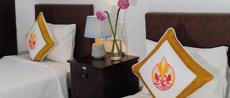 Ein Hotelzimmer mit zwei Betten, einem Nachttisch mit Lampe, einer Vase mit Blumen und dekorativen Kissen.