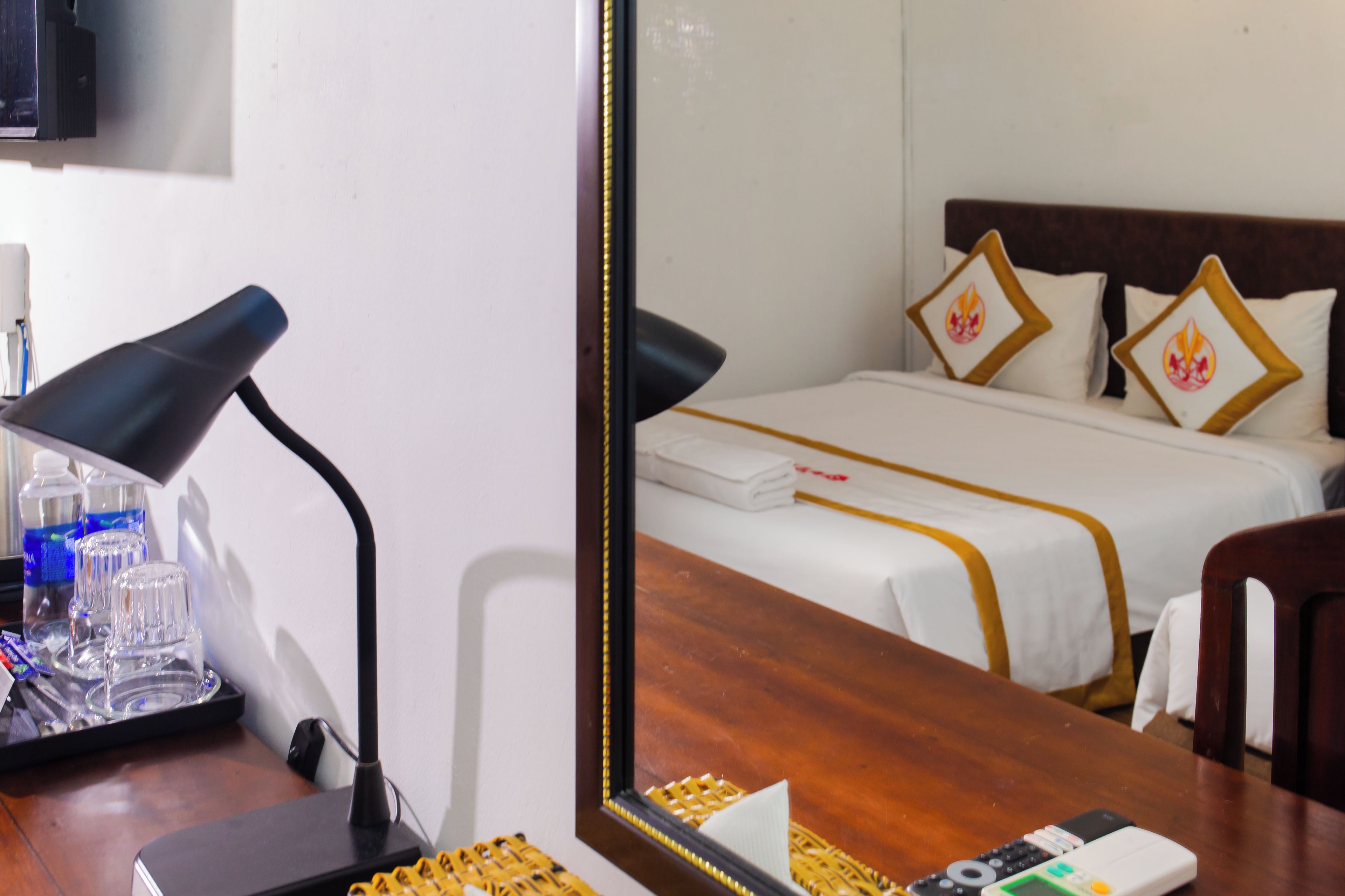 Habitación de hotel con cama, un escritorio con lámpara y un espejo que refleja el espacio.