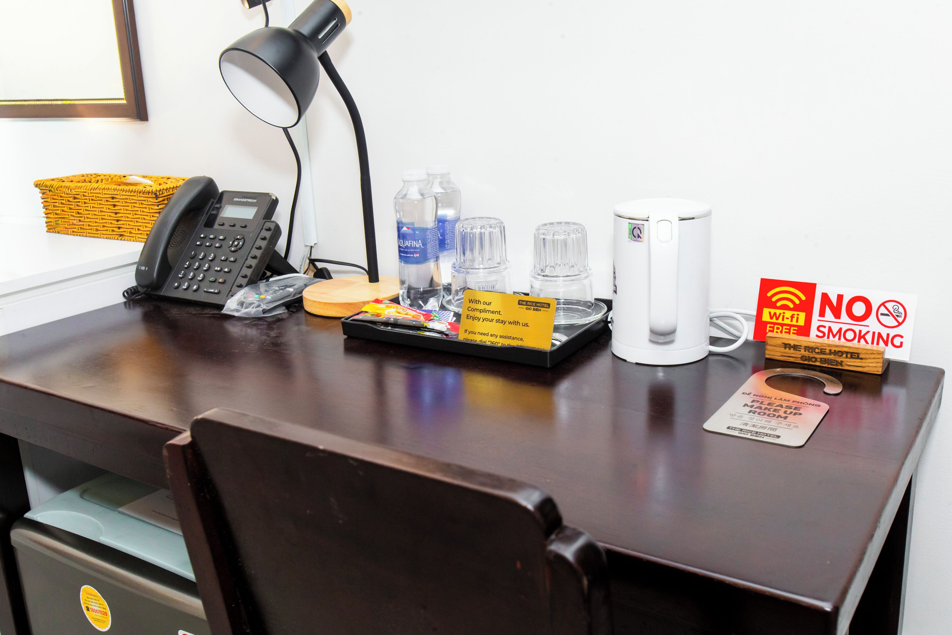 A hotel desk with a telephone, water bottles, a tray with snacks, a 'NO SMOKING' sign, and a 'Wi-Fi FREE' sign.