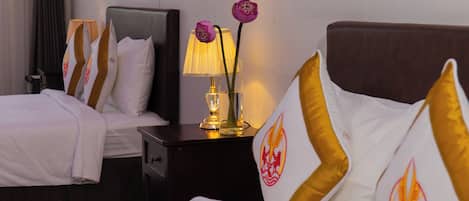 A hotel room with two beds, a nightstand with a lamp, and decorative pillows.