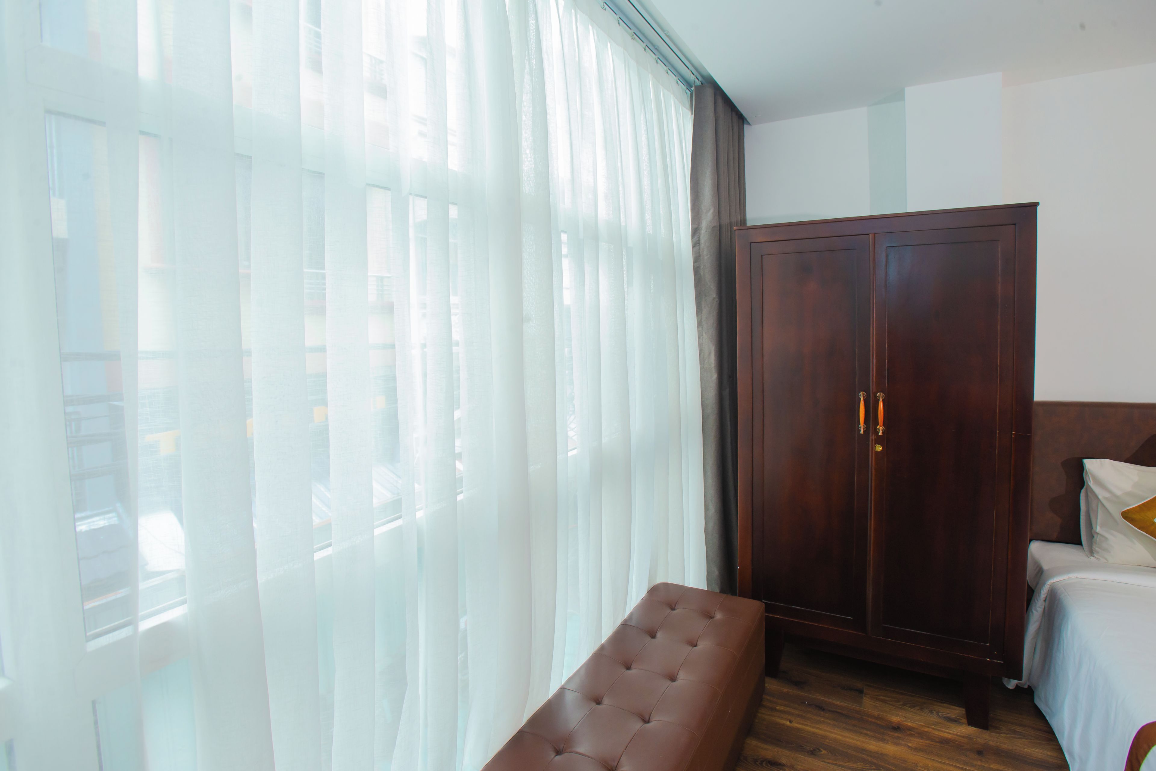 A bedroom with a bed, a bench, a wardrobe, and sheer curtains.