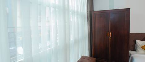 A bedroom with a bed, a bench, a wardrobe, and sheer curtains.