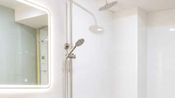 A modern bathroom with a white sink, mirror, and toilet, and a shower with a handheld showerhead.