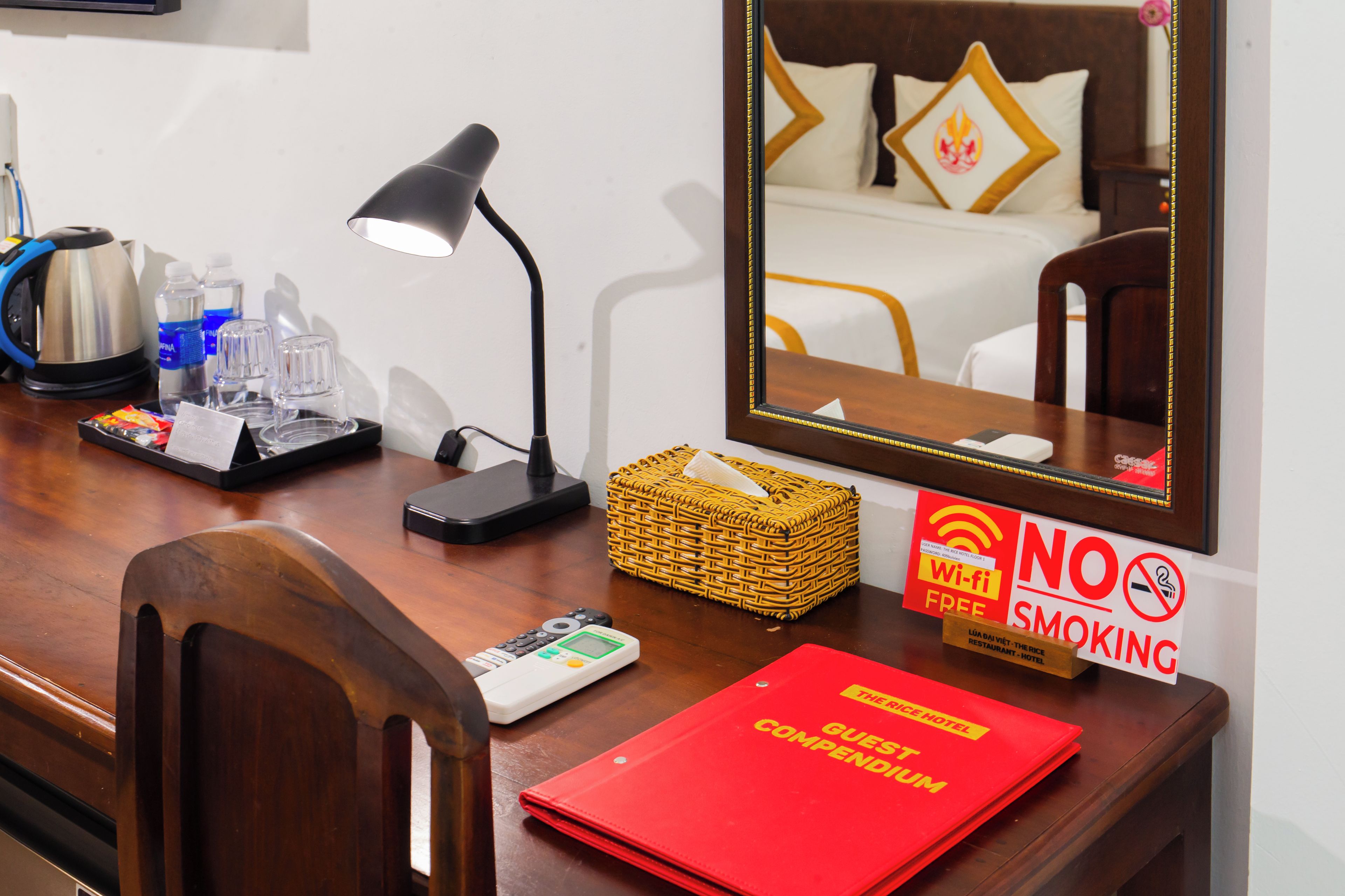 Habitación de hotel con escritorio, lámpara, tetera, cesta, cartel de no fumar y señal de Wi-Fi gratuito.