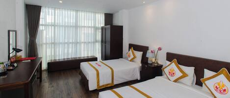 A hotel room with two beds, a desk, a bench, and a large window with curtains.