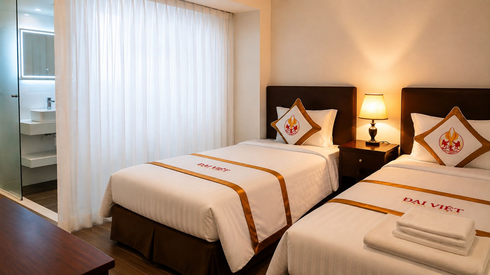 A hotel room with two beds, a nightstand with a lamp, a bathroom with a mirror, and a wooden floor.