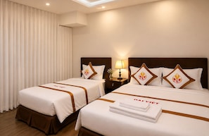 A hotel room with two beds, each with a pillow featuring a flame emblem, a nightstand with a lamp, and a window with vertical blinds. - The Rice Hotel - Bui Vien (Ho Chi Minh City)
