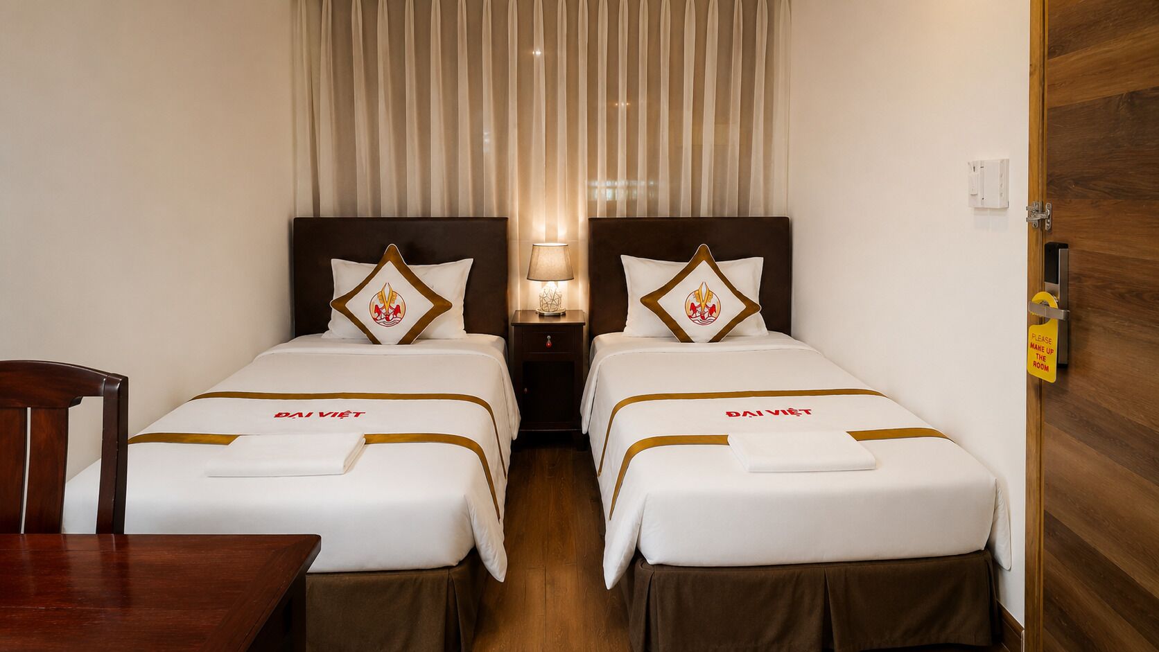 A hotel room with two beds, a nightstand, a lamp, and a wooden door.