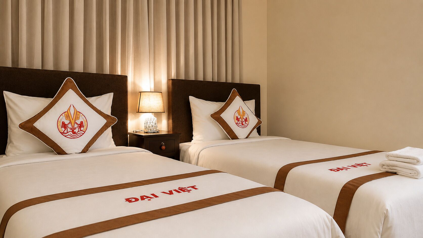 A hotel room with two beds, each with a brown headboard and white bedding. There is a nightstand with a lamp between the beds.