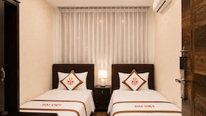 Et hotelværelse med to senge, hver med en 'DAI VIET' pude, et natbord med en lampe, og en trædør.