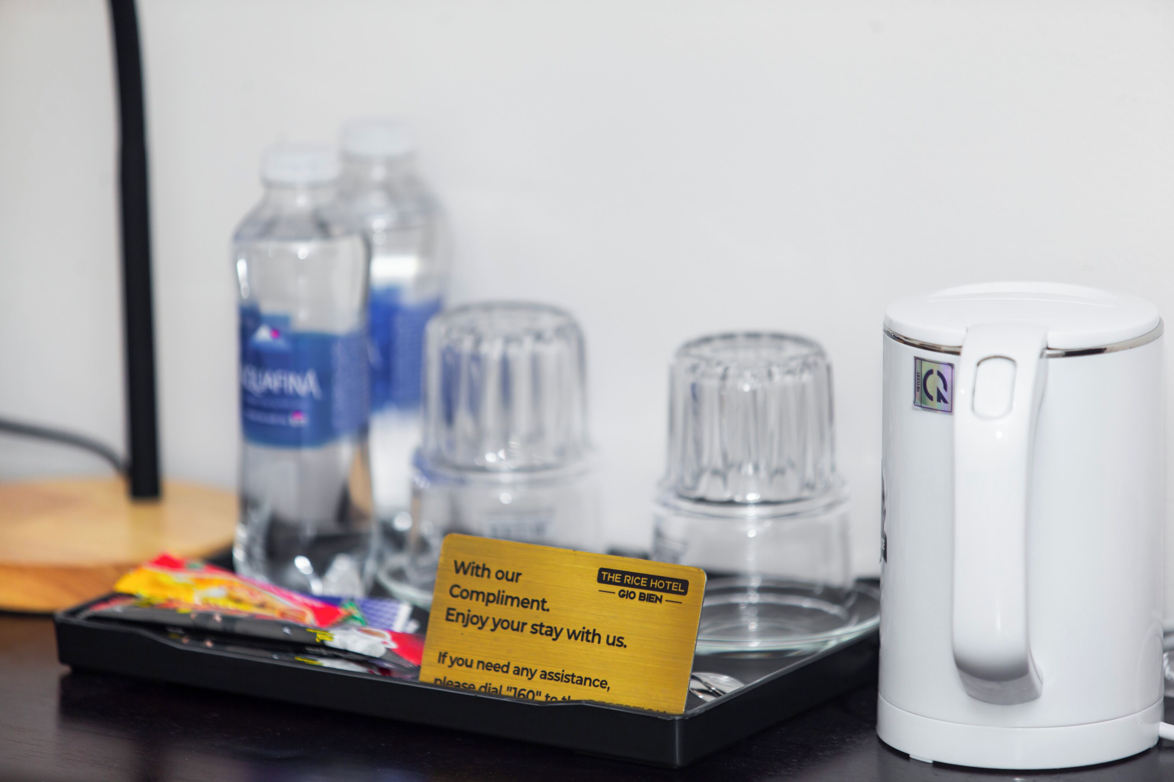Habitación de hotel con una bandeja que contiene una tarjeta, dos botellas de agua, una tetera blanca y una bandeja de aperitivos.