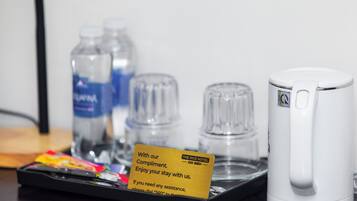 Habitación de hotel con una bandeja que contiene una tarjeta, dos botellas de agua, una tetera blanca y una bandeja de aperitivos.