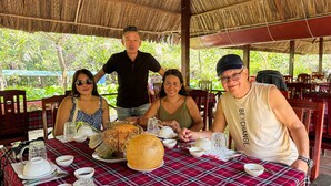 A group of people dining at an outdoor restaurant with a thatched roof, surrounded by lush greenery. - The Rice Hotel & Tour - 40 Bui Vien No 9 (Ho Chi Minh City)