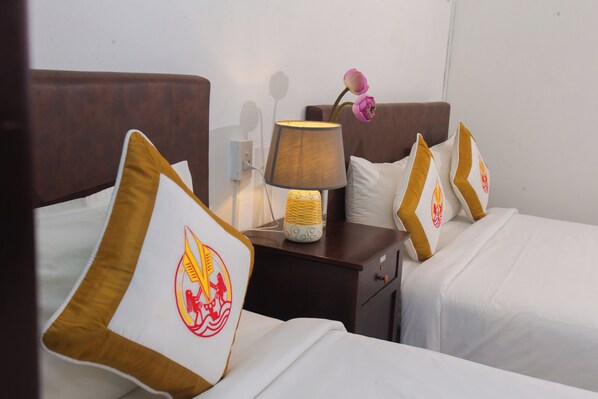 Quarto de hotel com cama, almofadas, mesa de cabeceira, abajur e espelho fixado na parede.