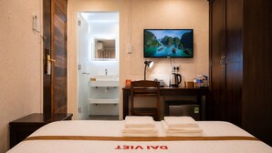 A hotel room with a bed, a desk with a chair, a TV mounted on the wall, and a bathroom visible through an open door. - The Rice Hotel & Tour - 40 Bui Vien No 9 (Ho Chi Minh City)
