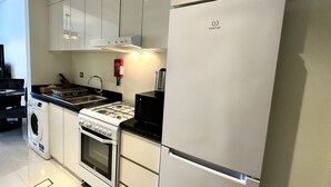 Una cocina moderna con armarios blancos, estufa de acero inoxidable, horno empotrado, un lavamanos y refrigerador blanco.