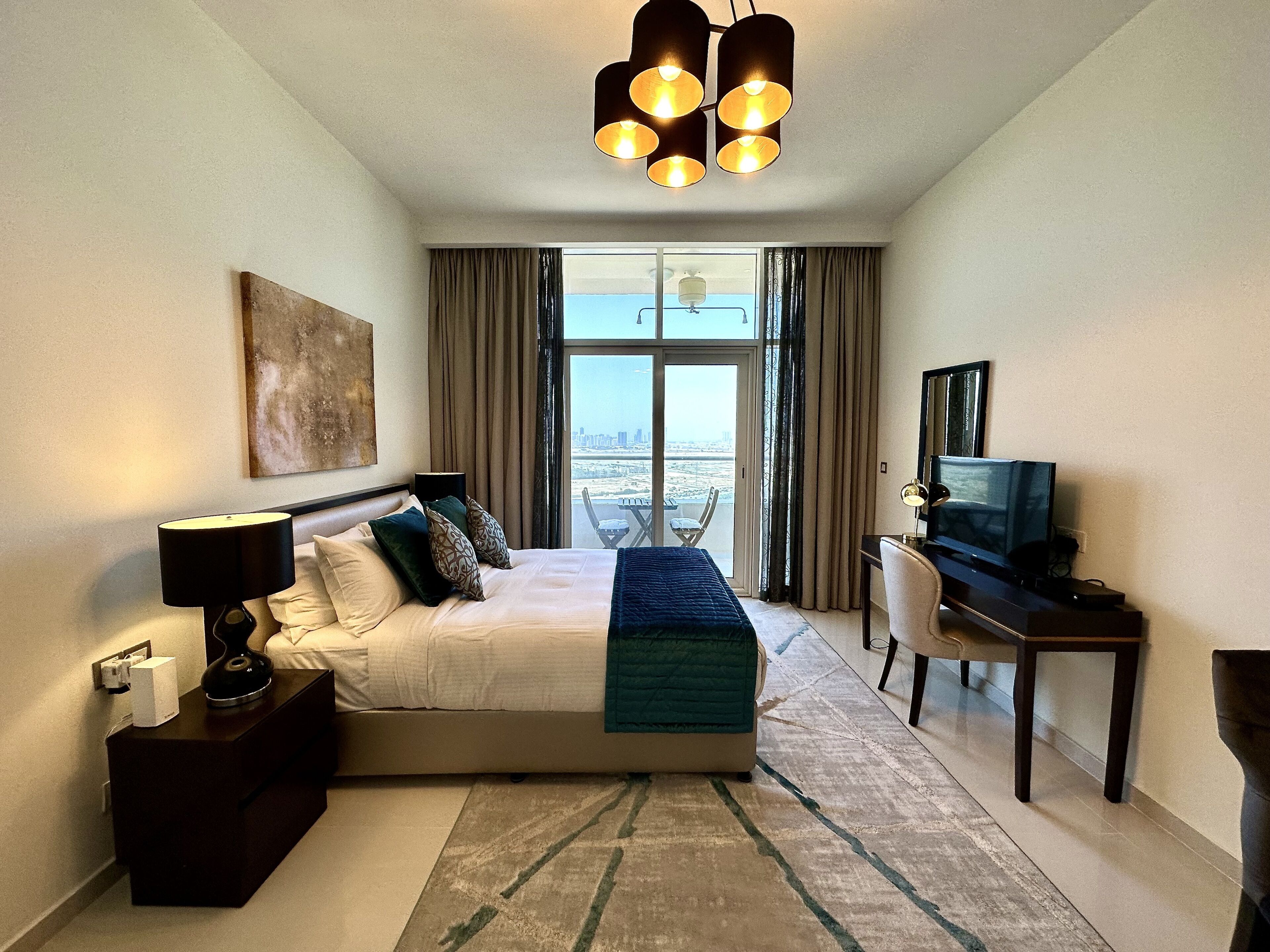 Une chambre d’hôtel avec un grand lit, un bureau avec une télévision, une vue sur la ville par la fenêtre et un lustre.