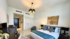 Habitación de hotel con cama, mesitas de noche, escritorio y una silla. Se observa un cuadro en la pared y una lámpara en el techo.