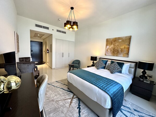 A hotel room with a bed, bedside tables, a desk, and a chair. There is a painting on the wall and a ceiling light fixture.