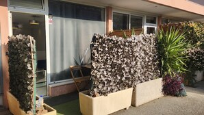 A building entrance with a metal gate, a wooden bench, and potted plants. - Logement Résidence (Antibes)