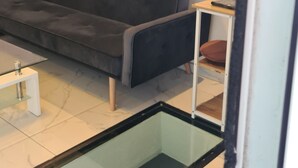 A modern living room with a dark grey sofa, a glass coffee table, and a small wooden side table. - Logement Résidence (Antibes)