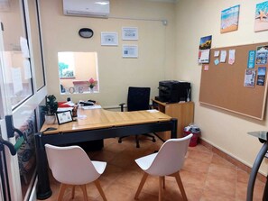 A conference room with a long table, two white chairs, a black office chair, a printer, and a bulletin board with various notices.