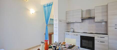 Una cocina compacta con electrodomésticos modernos, un comedor con una mesa dispuesta para el desayuno y una cortina azul entreabierta.